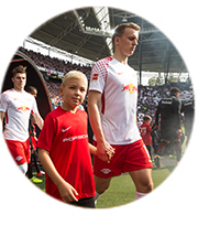 2 Fußballspieler laufen mit einem Kind im Stadion ein