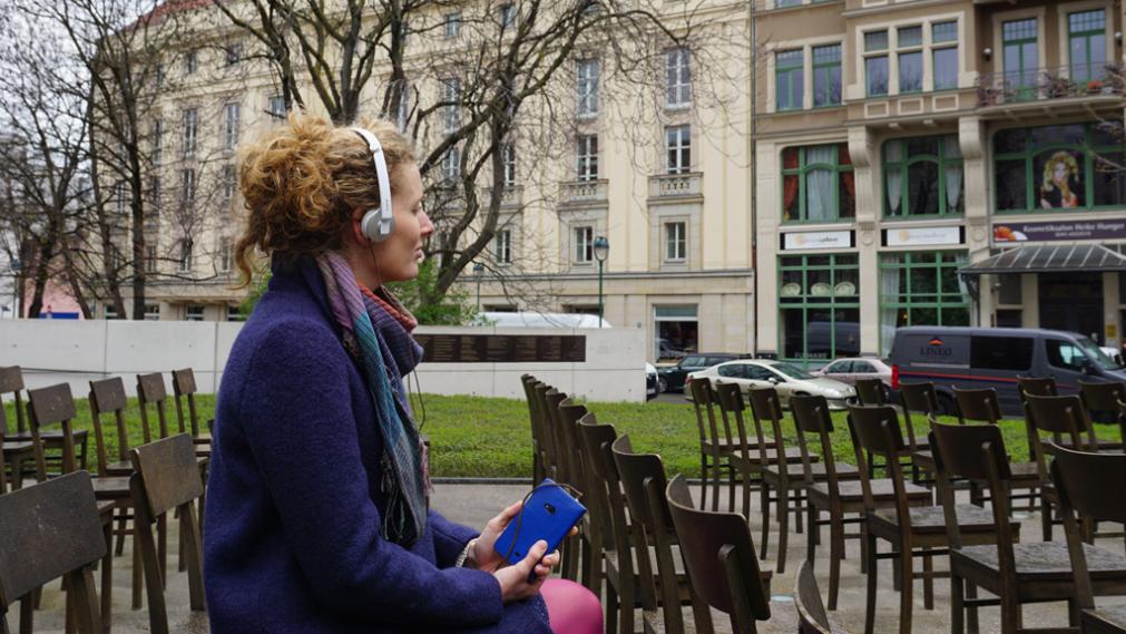 Junge Frau hört Audiopodcast am Synagogendenkmal